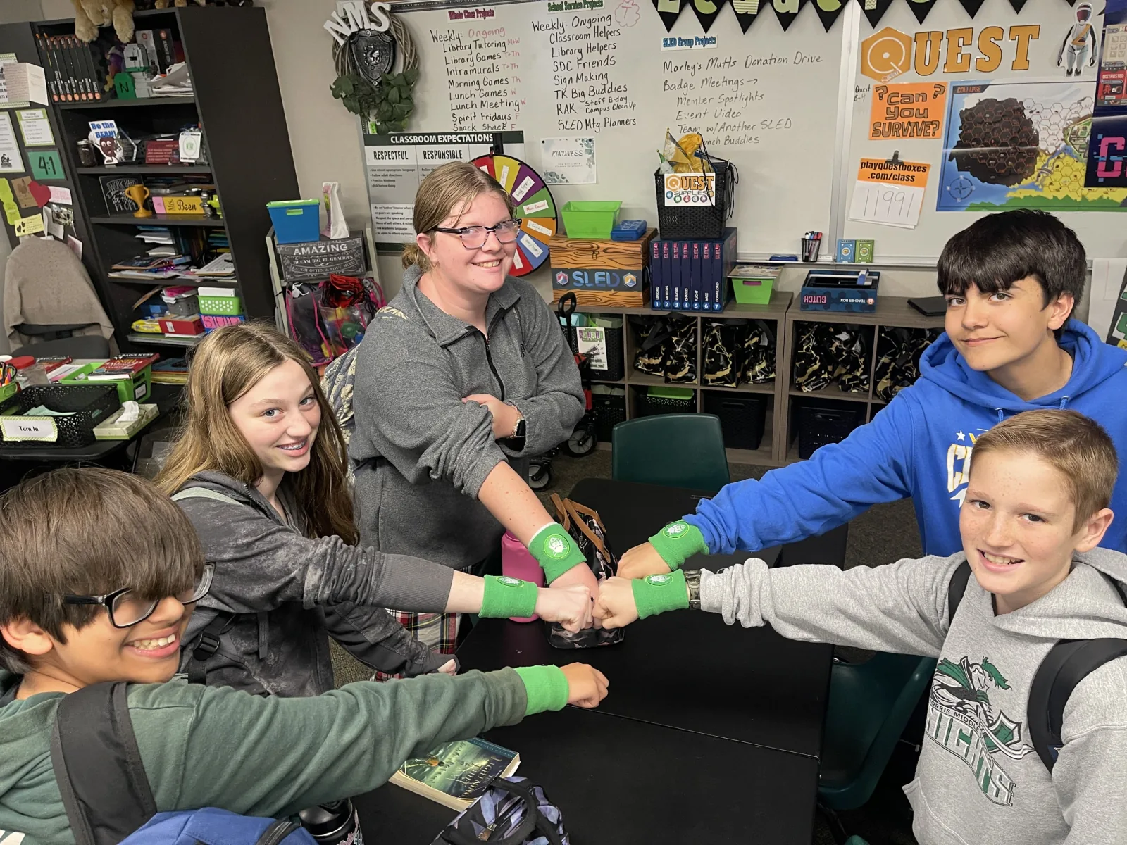 Students and a teacher fist-bump in a circle wearing matching wristbands